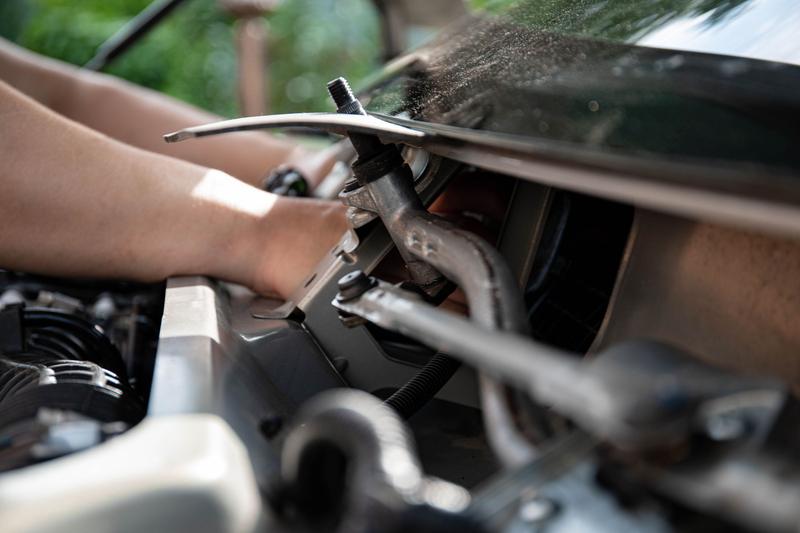 Nahaufnahme von Händen mit Werkzeug an einem Bauteil im Motorraum.