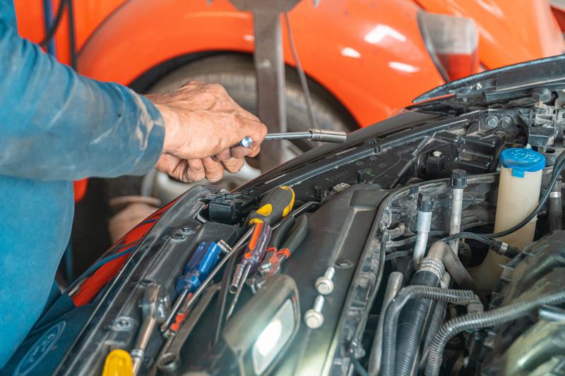 Hände mit Steckschlüssel arbeiten im Motorraum, Schraubendreher liegen bereit.