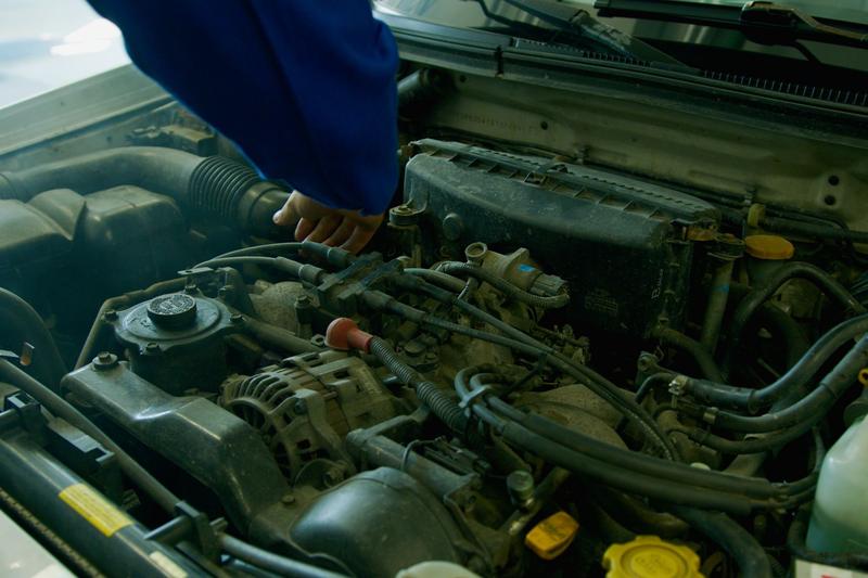 Blick in einen geöffneten Motorraum, eine Hand arbeitet an den Anbauteilen.